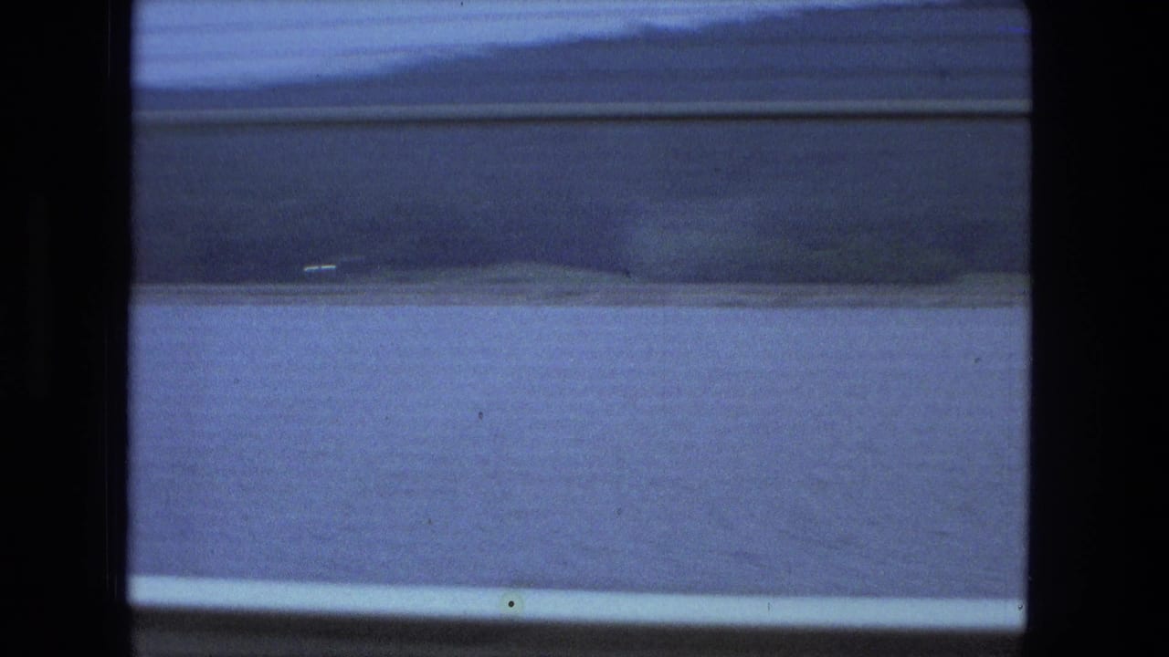 Small boat crossing a blue lake beyond dark vertical window or frame edges.