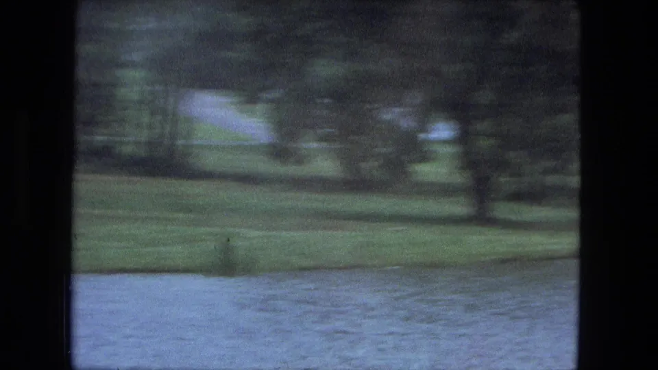 1974 Fort Wayne home-movie view of wet roadway, water, grass, and trees from a moving vehicle.
