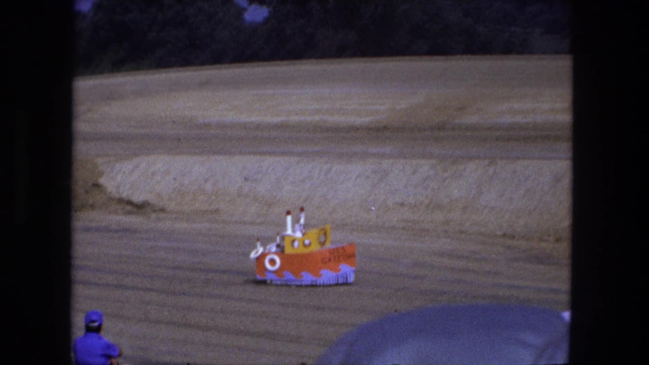 Small orange and yellow USS CATFISH boat vehicle crossing a sandy field.
