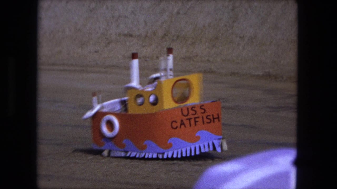 Colorful USS Catfish model boat seen closer on sandy ground.