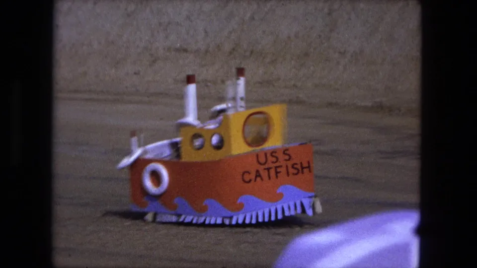 The handmade USS Catfish model shows its orange hull, yellow cabin, white stacks, and life ring in 1974 home-movie footage.