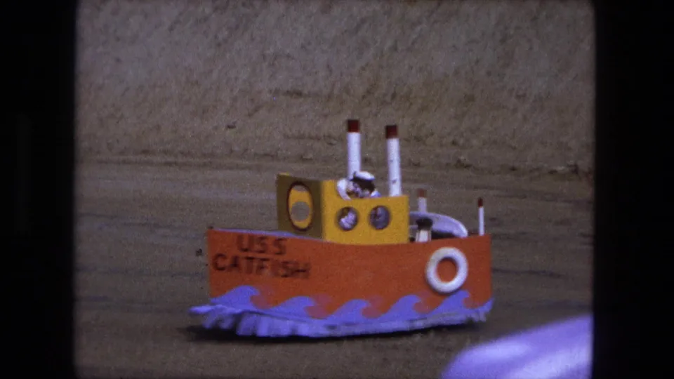 1974 8mm frame with the USS Catfish model partly cropped, showing painted waves, cabin details, and soft film grain.