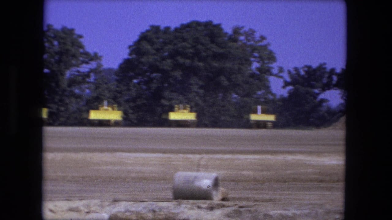 1974 Fort Wayne frame with yellow construction equipment near trees and a concrete pipe lying in the foreground of the graded site.