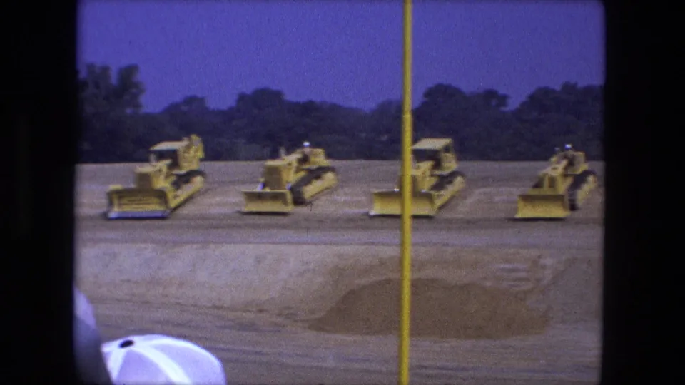 1974 Fort Wayne 8mm frame showing several yellow bulldozers or earthmovers parked in a row on a broad dirt worksite.
