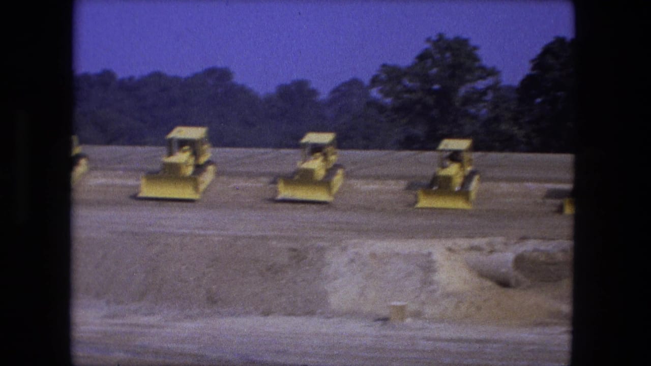 Several yellow loaders spread across a dirt construction site with trees in the background.