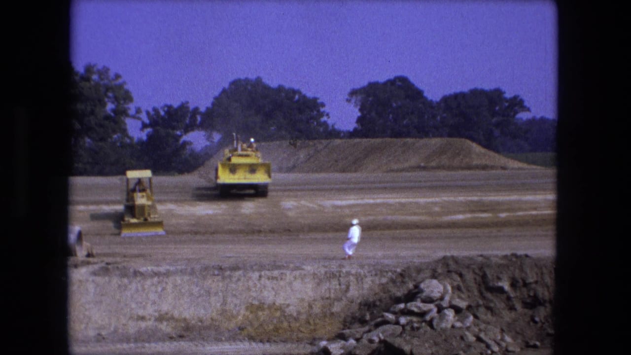Yellow construction equipment works across a wide dirt field with workers nearby.