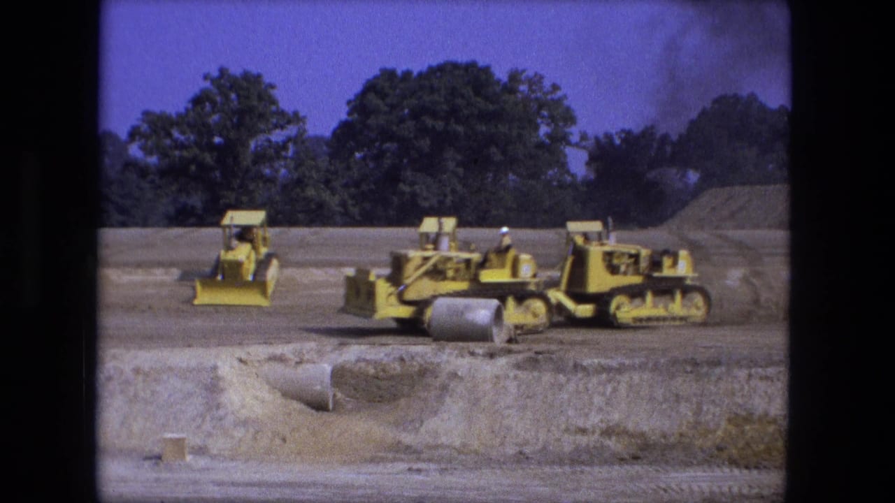 Several yellow bulldozers and loaders line up on a graded construction site.