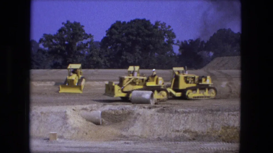 1974 Fort Wayne construction site with multiple yellow bulldozers or loaders positioned near a culvert opening and earth piles.