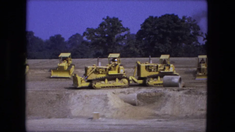1974 Fort Wayne construction footage showing yellow bulldozers and loaders beside a culvert or pipe opening on a graded site.