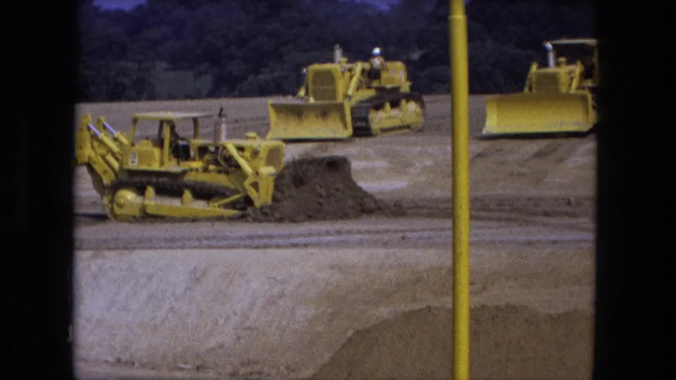 1974 Fort Wayne 8mm frame showing several yellow bulldozers moving earth at a large graded excavation site.