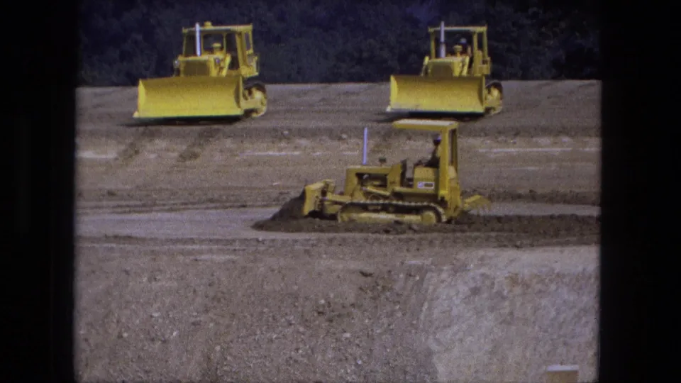 1974 Fort Wayne 8mm frame showing yellow bulldozers on a graded dirt site with a smaller tracked machine in front.
