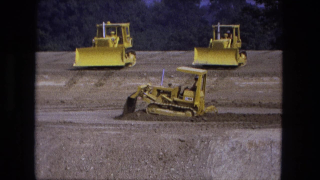 Small yellow tracked machine pushes dirt while larger bulldozers sit behind it.