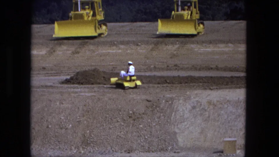 1974 Fort Wayne construction-site frame with a worker on a small yellow tracked machine and two larger dozers in the background.
