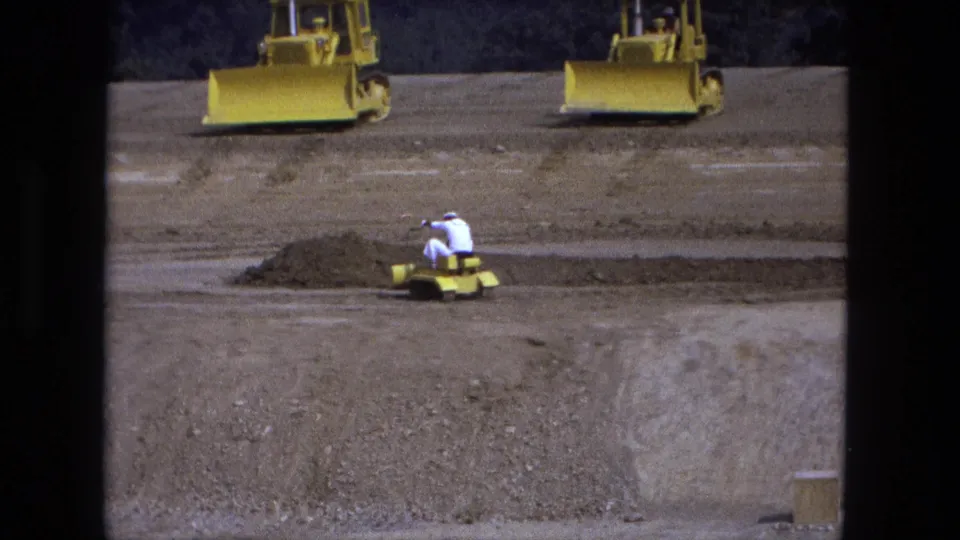 1974 Fort Wayne 8mm frame showing a worker on a small yellow dozer grading dirt, with two larger yellow bulldozers in the background.