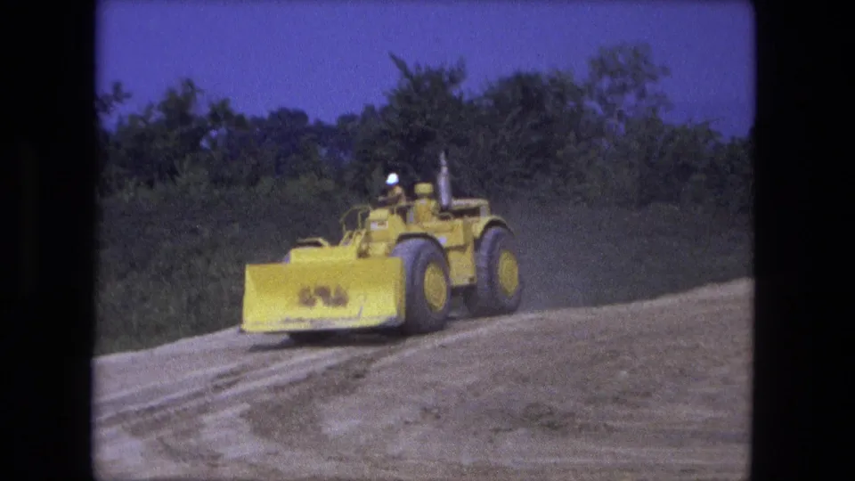 The earth mover crosses the Fort Wayne work site, with its blade forward and the operator seated behind it.