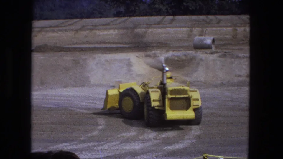 Rear view of the earth mover driving through a graded basin, with a pipe-like cylinder visible in the background.