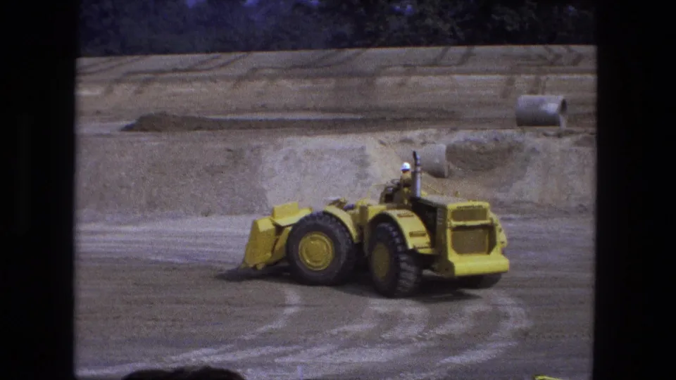 1974 Fort Wayne 8mm frame showing a yellow front-end loader working on a large dirt construction site.