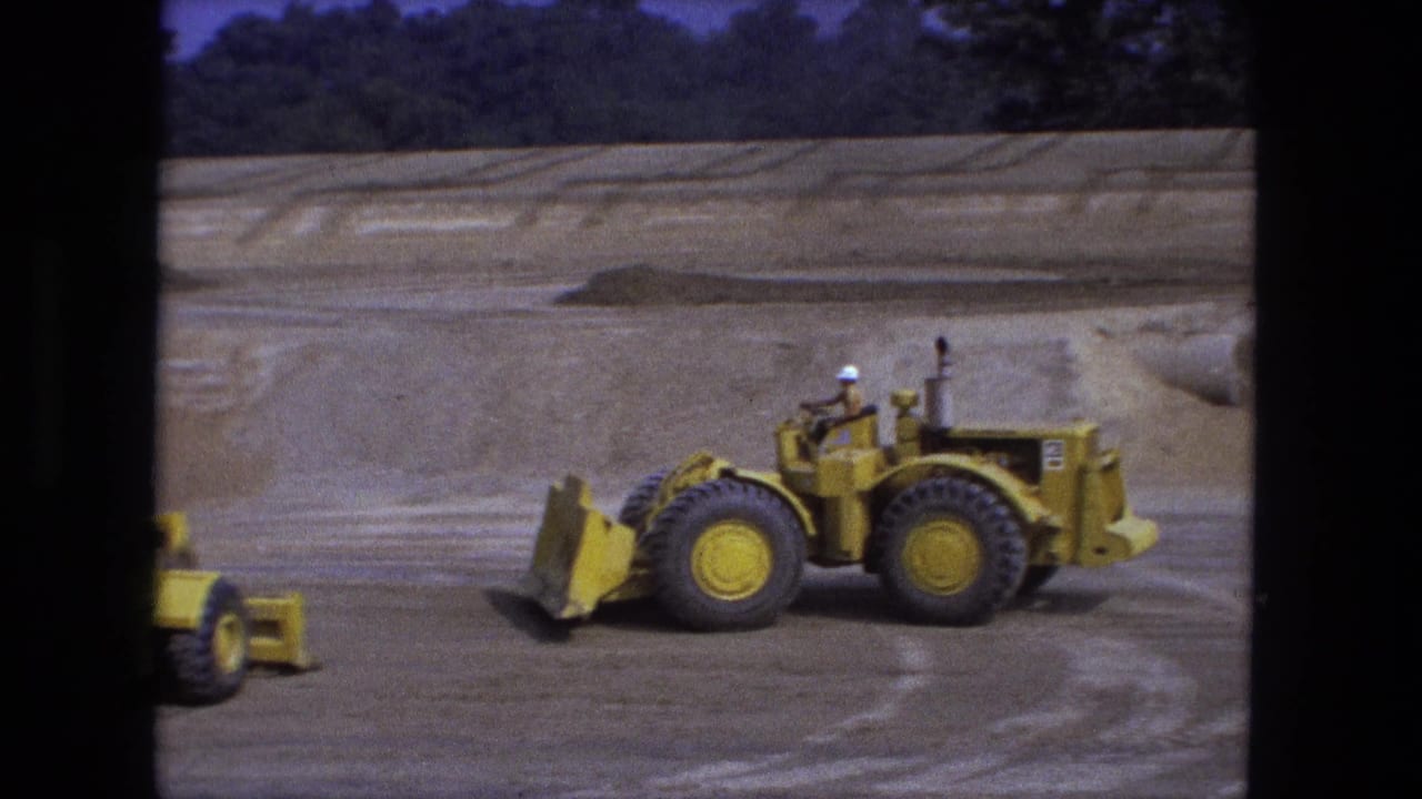 1974 Fort Wayne 8mm frame with a hard-hatted operator on a yellow loader at an outdoor construction site.