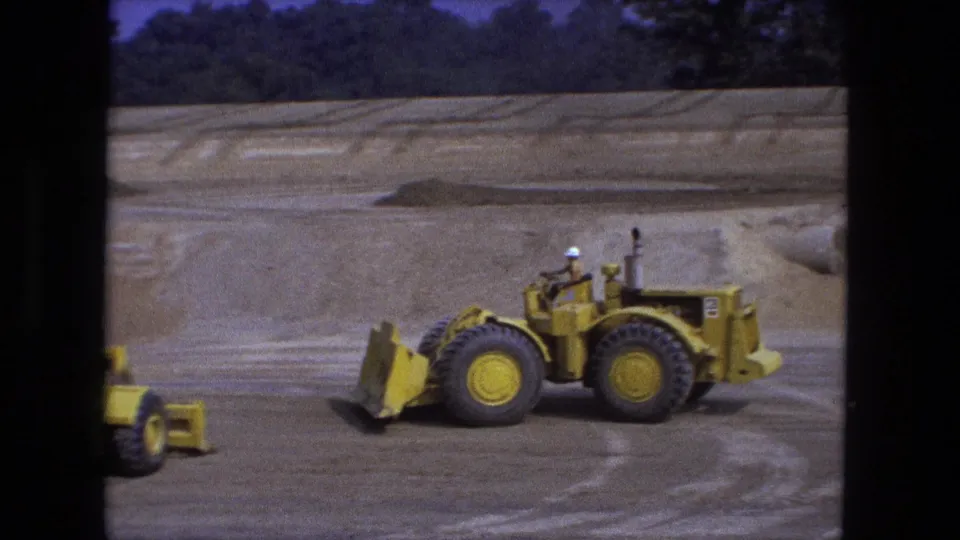 1974 Fort Wayne 8mm frame with a hard-hatted operator on a yellow loader at an outdoor construction site.
