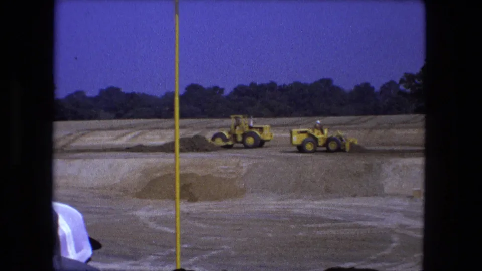 Wide 1974 Fort Wayne 8mm frame of yellow earthmoving vehicles spread across a graded dirt site.