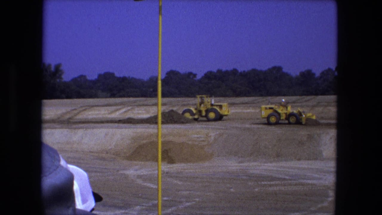 Two yellow loaders work across a dirt construction site behind a vertical pole.