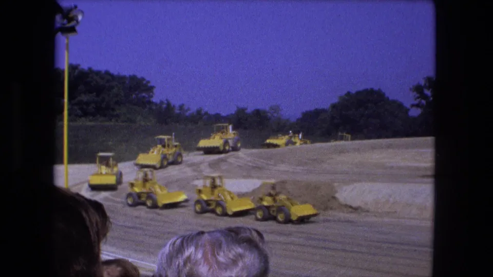 1974 Fort Wayne frame with multiple yellow tractors and bulldozers arranged across a large dirt site under a blue sky.