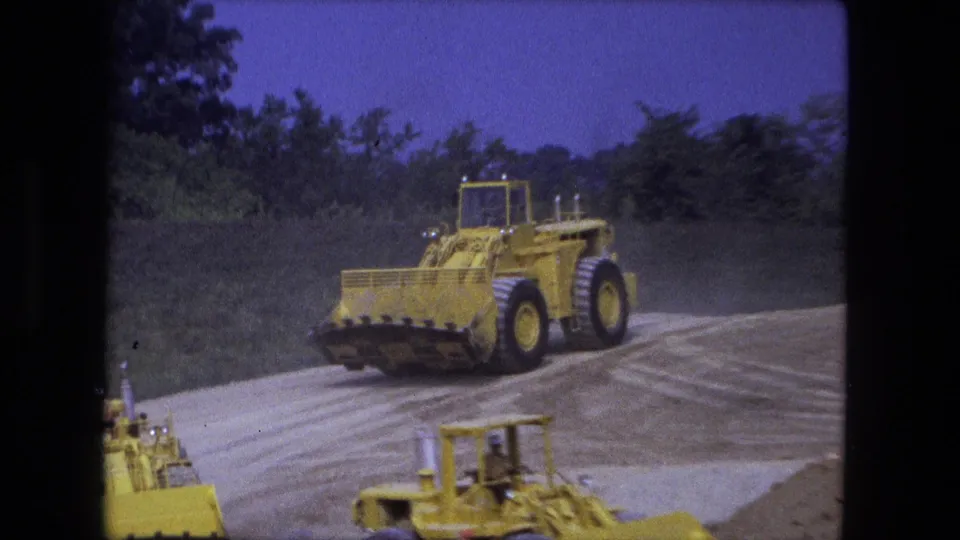 Fort Wayne, Indiana 1974 frame with a large yellow loader moving toward the camera on a graded dirt track at a public worksite.