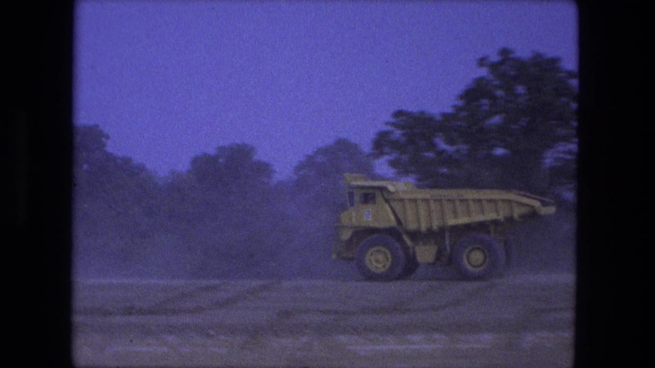 Large yellow dump truck near the right edge of a dusty worksite frame.