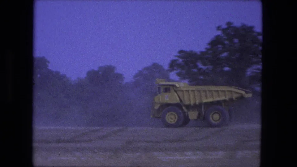 1974 Fort Wayne 8mm frame with a large yellow off-road dump truck passing through a dusty construction area.