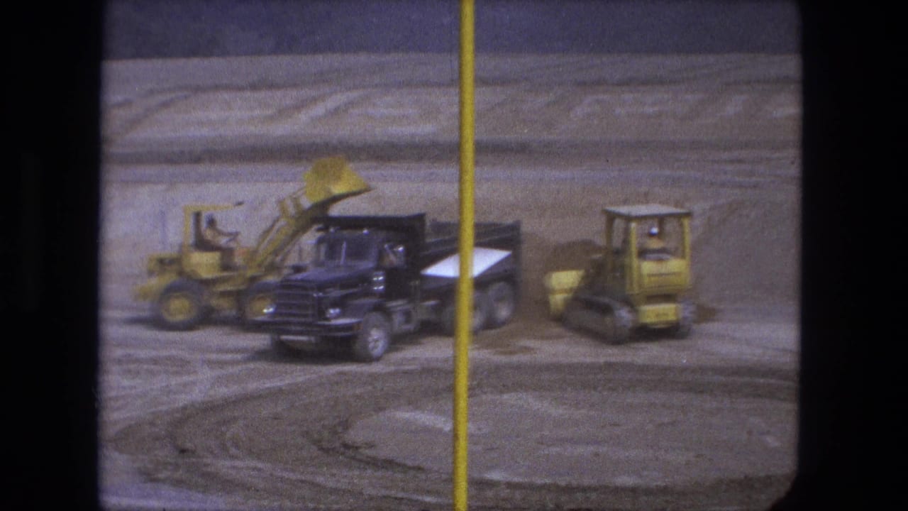 Black dump truck beside yellow loaders on a dusty construction site.