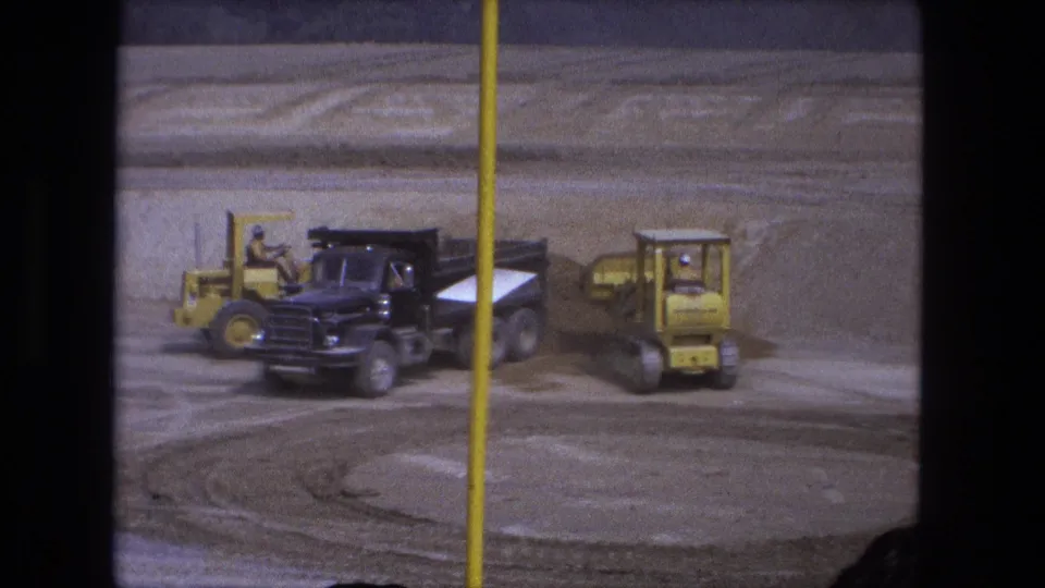 Yellow loaders and a black dump truck work around visible tire tracks in this 1974 Fort Wayne 8mm construction scene.