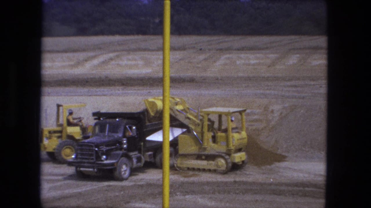 Yellow loader works beside a black dump truck at an excavation site.