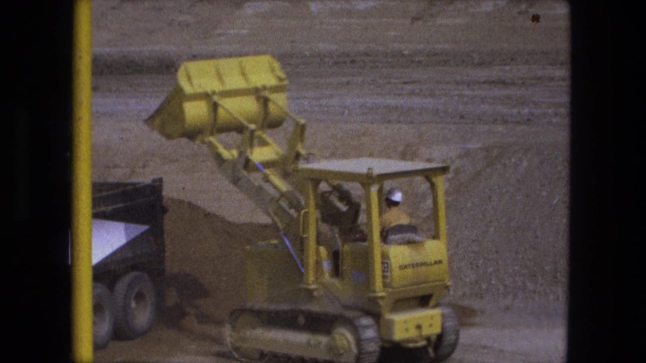 Yellow Caterpillar loader tips its bucket over a truck bed during 1974 excavation work in Fort Wayne.