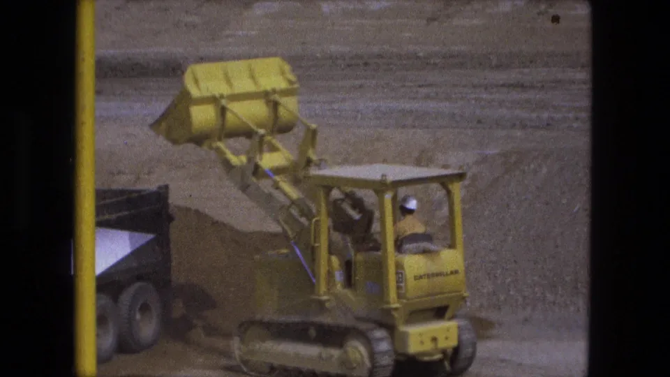 Yellow Caterpillar loader tips its bucket over a truck bed during 1974 excavation work in Fort Wayne.