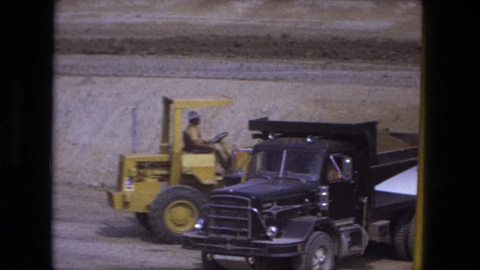 1974 Fort Wayne construction view with a yellow loader beside a black dump truck on an open earthwork site.
