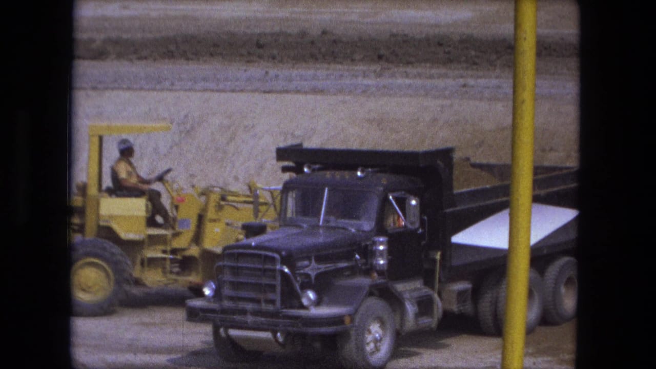Yellow construction loader beside a black dump truck on a dusty worksite.
