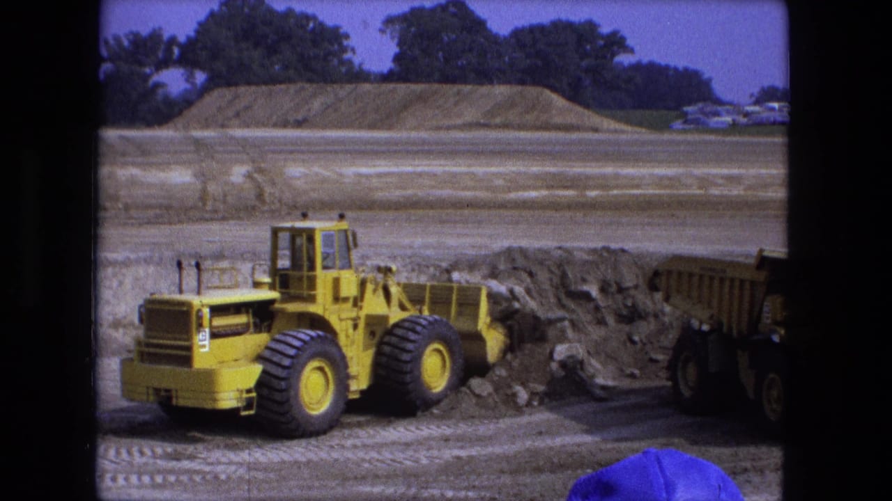 Yellow front-end loader beside a dirt pile at an open construction site.