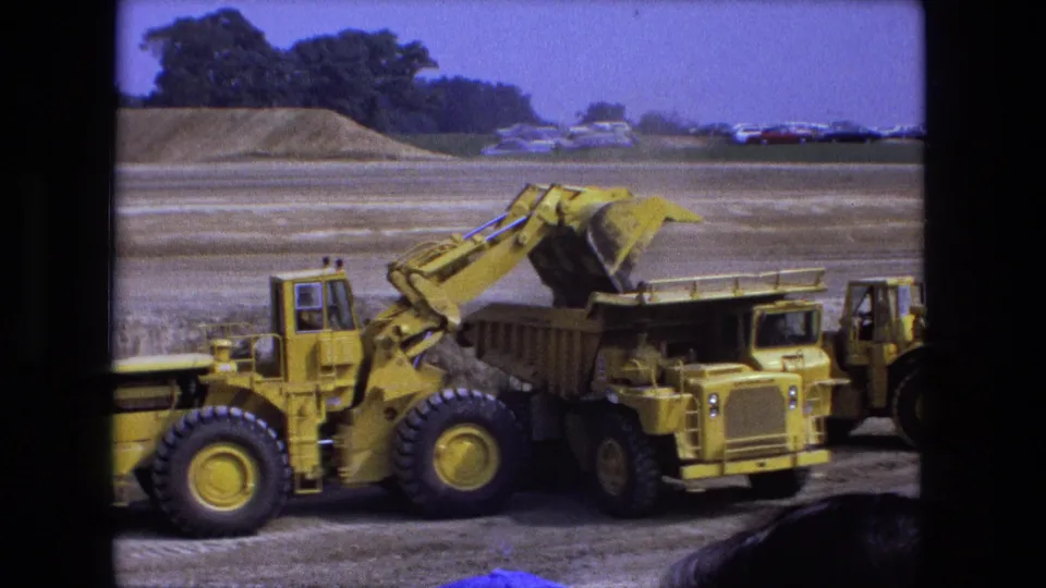 Final frame of the 1974 Fort Wayne worksite shows the loader near the dump truck, with a second machine partly visible and a spectator head at the bottom edge.