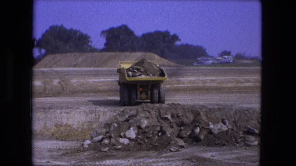 1974 Fort Wayne 8mm frame showing the dump truck from behind with a load of dirt near a rocky foreground pile.