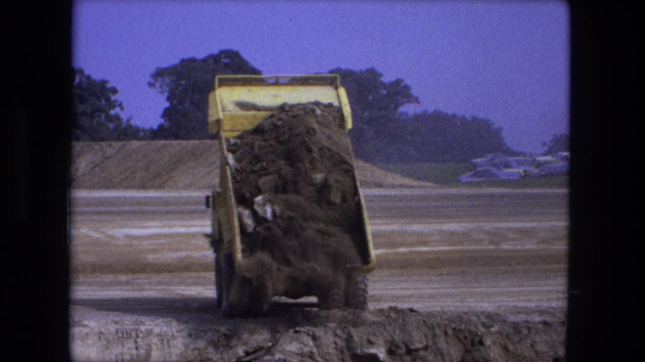 Yellow dump truck unloads dirt and rocks onto a dusty roadbed.