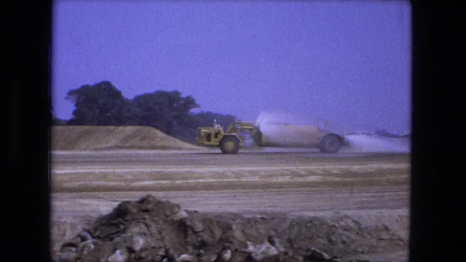 A yellow water truck sprays down the dusty road construction site in Fort Wayne, Indiana, after the dump truck unloads.
