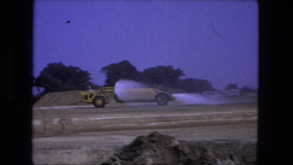 The yellow water truck moves across the Fort Wayne construction site as a low spray cloud follows over the road surface.