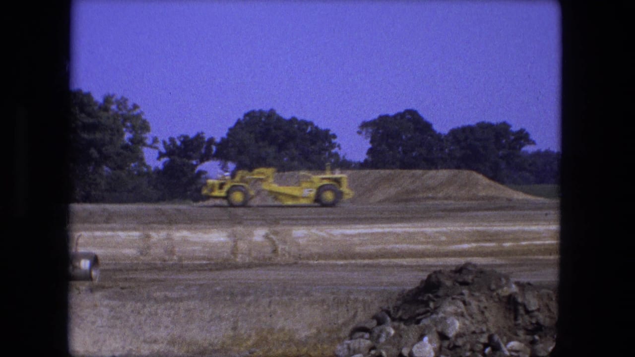 Yellow grader passes a low mound of soil on an open construction site.