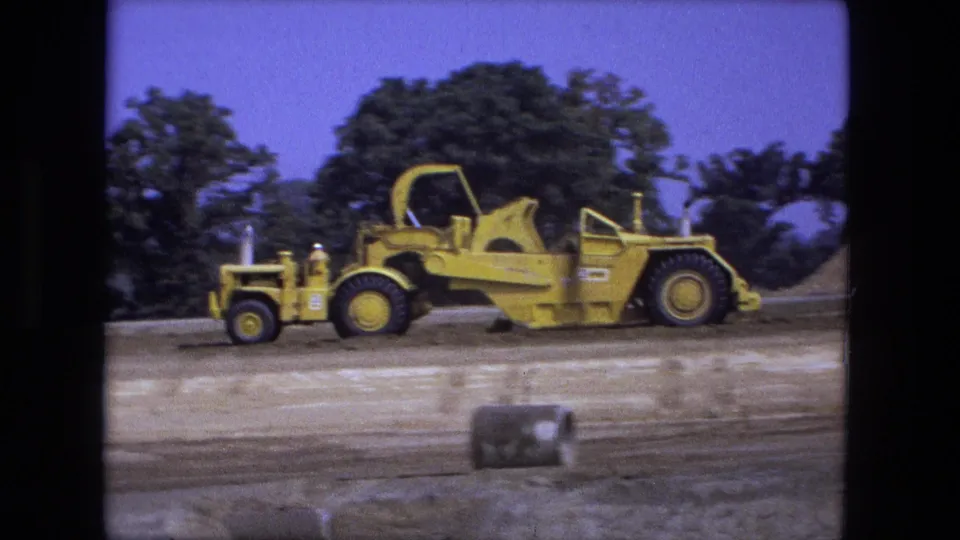 Fort Wayne, Indiana 1974 8mm frame of yellow construction machinery on exposed dirt with trees in the background.