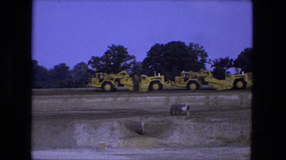 1974 Fort Wayne 8mm frame with multiple yellow earthmoving machines on a rural construction site.