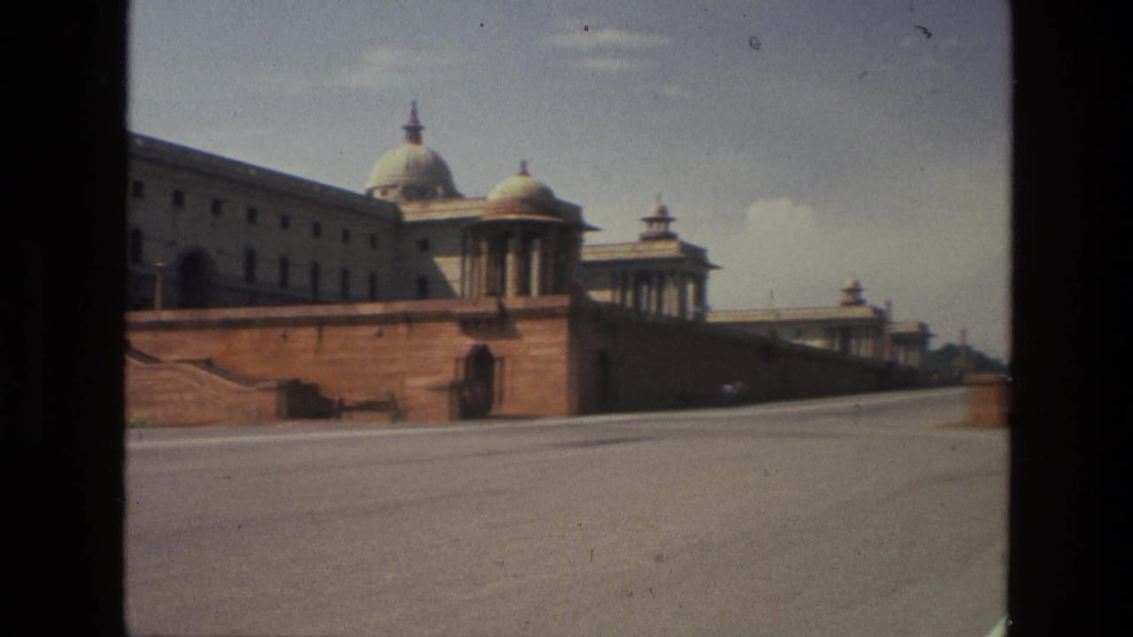 1974 India home-movie frame showing a monumental domed building behind red sandstone walls, viewed from across a broad road.