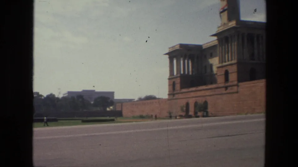 1974 India 8mm frame showing a broad paved area and a large formal red-toned civic building beyond a lawn.