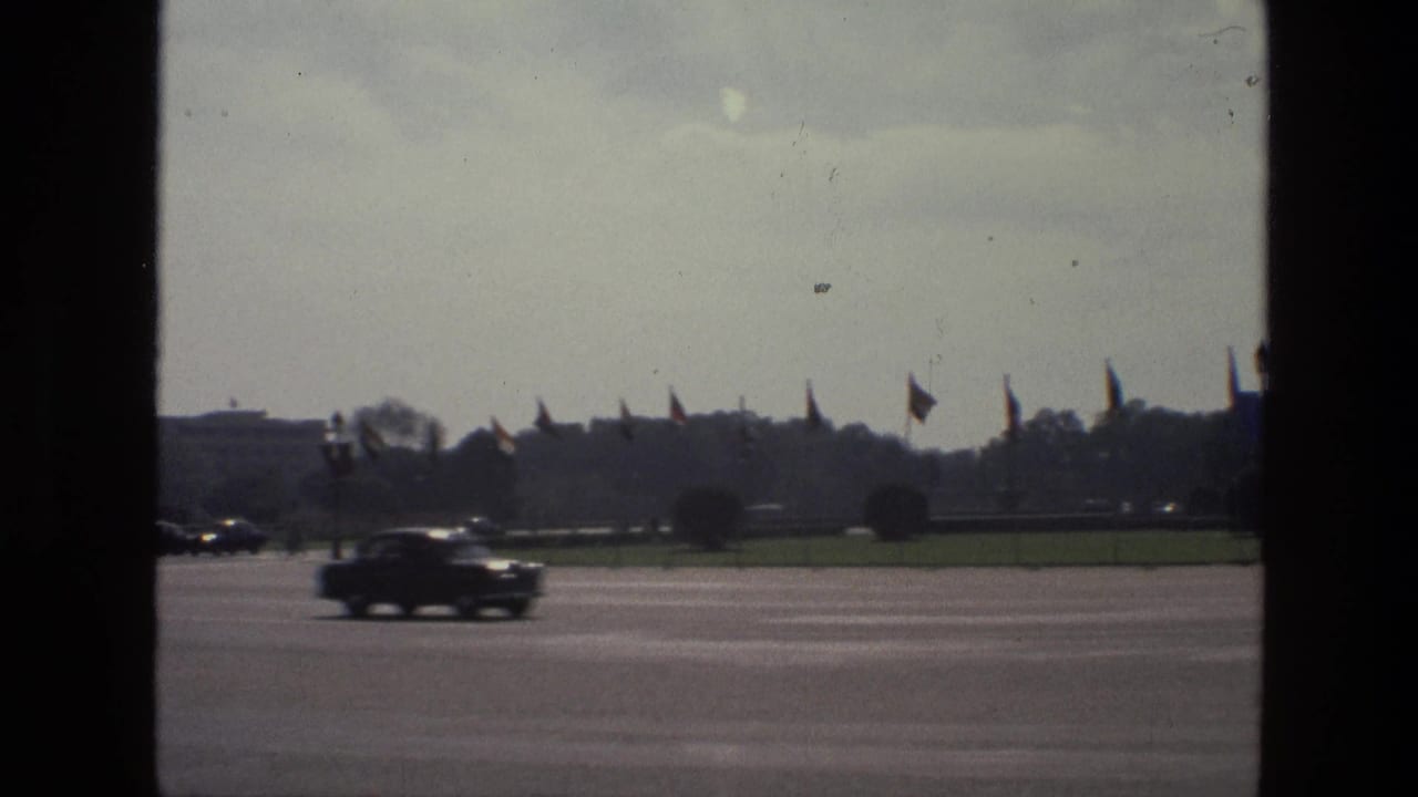 Wide road seen through a dark window frame with cars passing and flags in the distance.