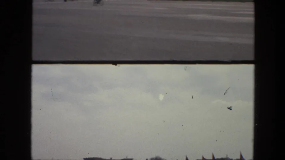1974 India 8mm frame with pale overcast sky, a low horizon, distant flag shapes, and dark window framing.
