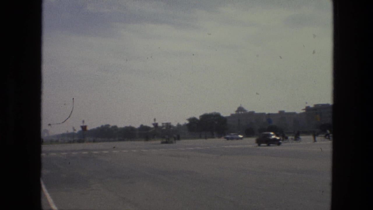 Wide road across a large public square with cars and distant buildings under a hazy sky.